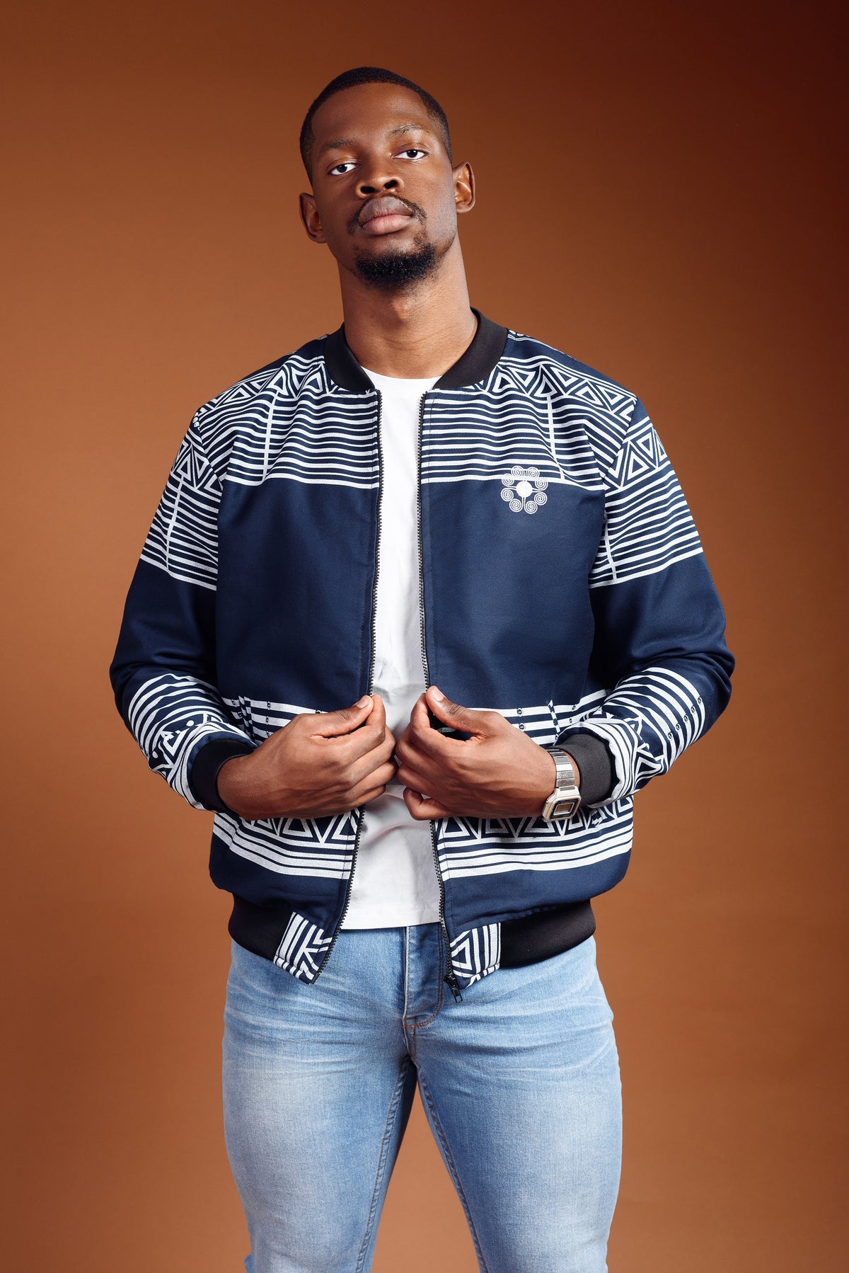 A man wearing a striped navy and white bomber jacket with a round embroidered logo on the chest.