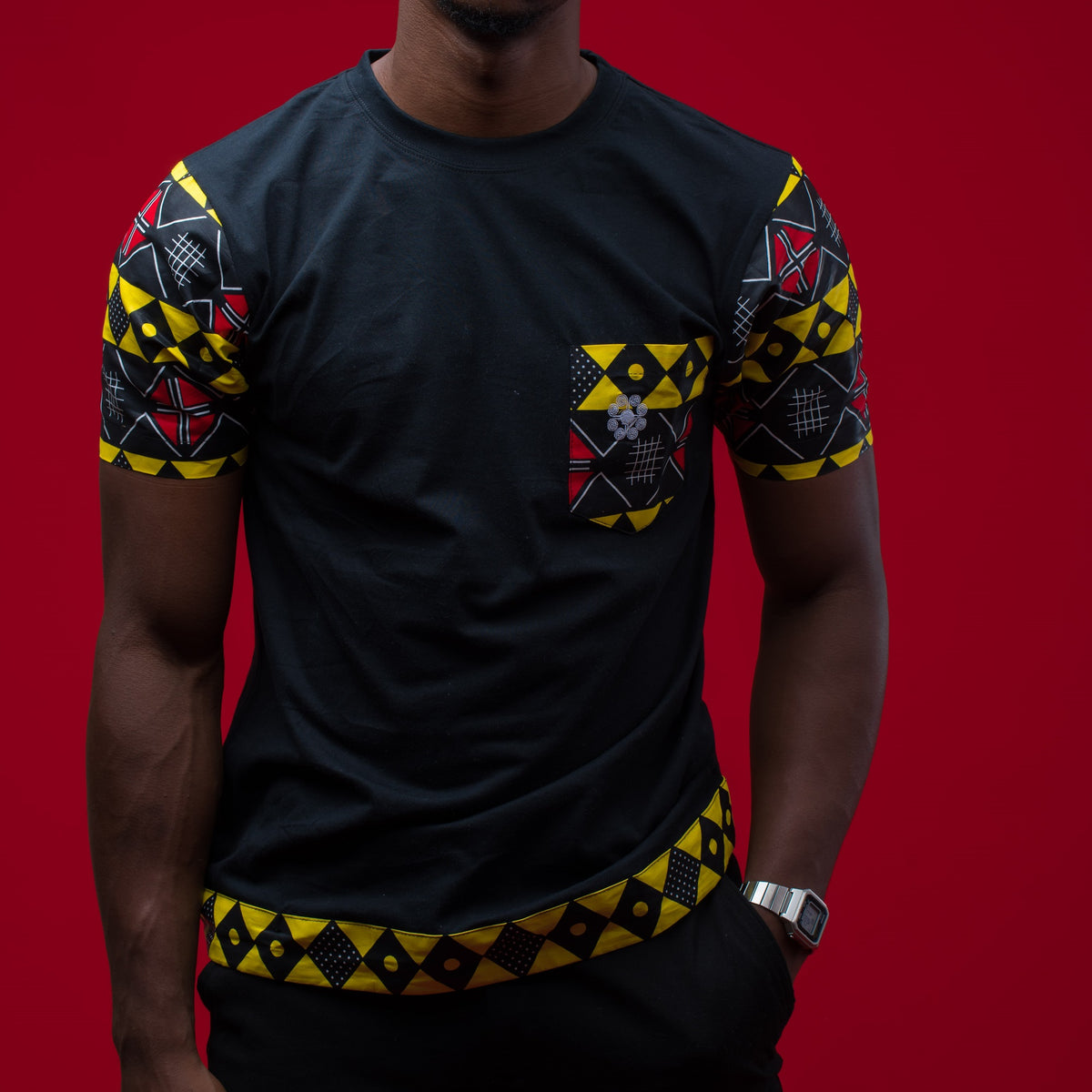 A male model wearing a black cotton T-shirt with geometric African print patterns on the sleeves and chest against a red background.